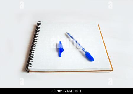 Öffnen Sie das Notizbuch mit einer leeren Seite, auf der ein blauer Stift und die Abdeckung entfernt ist, um mit dem Schreiben zu beginnen. Stockfoto