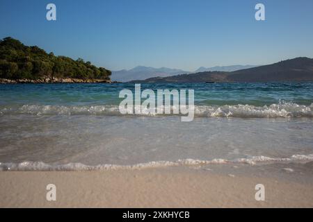 Vormittagslandschaft der Sandküste mit dem Ionischen Meer und der Insel Ksamil in Südalbanien. Albanische Landschaft mit Wasser und Bergen während des Sommervormittags. Stockfoto