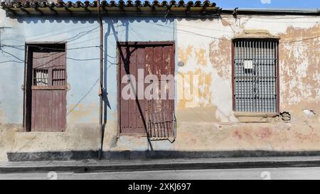 523 einstöckige, baufällige Kolonialhäuser zum Verkauf an der Westseite der Calvario Street mit abgebrochenen, lackierten hellblau-weißen Fassaden. Santiago-Kuba Stockfoto