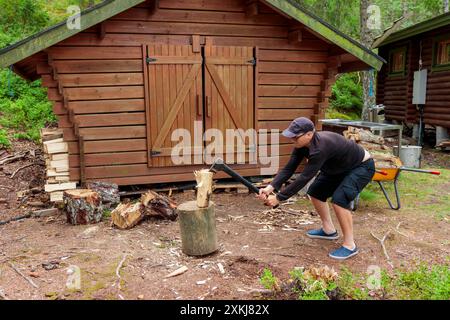 Männlich in schwarzen Tüchern auf dem Land Holz mit Stahlaxt hacken, Landlandschaft mit Holzfäller, Brennholz für den Winter sammeln. Holzschutz und Stockfoto