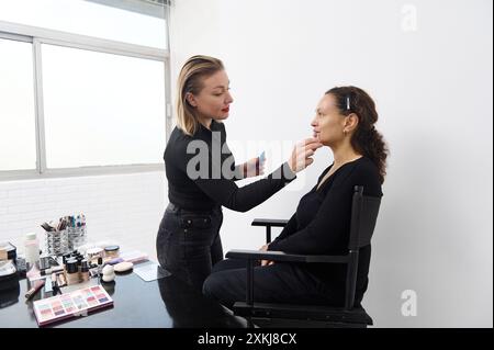 Ein professioneller Make-up-Künstler trägt Lippenstift sorgfältig auf einen älteren Kunden in einem hellen Studio-Setting auf und betont dabei geschickte Make-up-Techniken und Klie Stockfoto