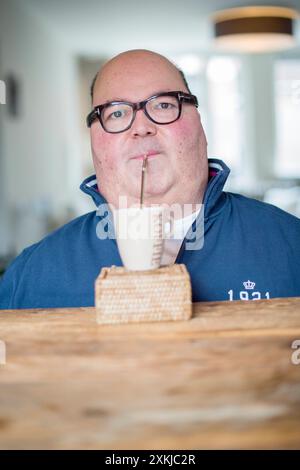 Mann trinkt Kaffee Mann mittleren Alters mit Muskeldystrophie und hängt vom Rollstuhl ab, trinkt seinen Kaffee durch einen Strohhalm. Tilburg, Niederlande. MRYES Tilburg Tuinstraat 47-12 Noord-Brabant Nederland Copyright: XGuidoxKoppesxPhotox Stockfoto