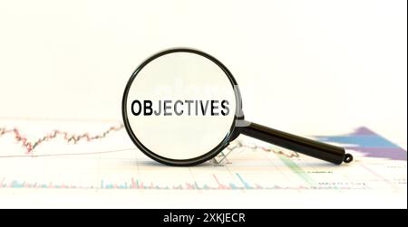 Vergrößerungsglas mit Textobjektiven auf Hintergrund mit Diagrammen. Geschäftskonzept. Vorderansicht. Zielsetzung. Stockfoto
