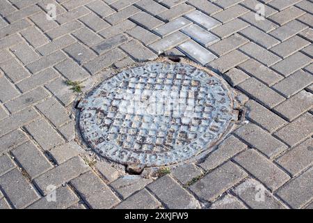 Auf einem Bürgersteig aus Ziegeln befindet sich ein runder Mannloch, der zwei verschiedene Materialien und Texturen in einer städtischen Umgebung vereint Stockfoto