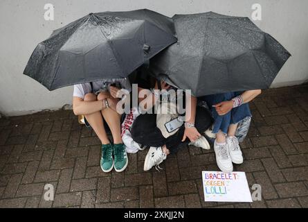 Hamburg, Deutschland. Juli 2024. Drei junge Fans sitzen beim Konzert des US-Sängers Taylor Swift vor dem Volksparkstadion unter ihrem Schirm. Es ist das vierte Konzert in Deutschland im Rahmen ihrer „Eras Tour“. Quelle: Christian Charisius/dpa/Alamy Live News Stockfoto