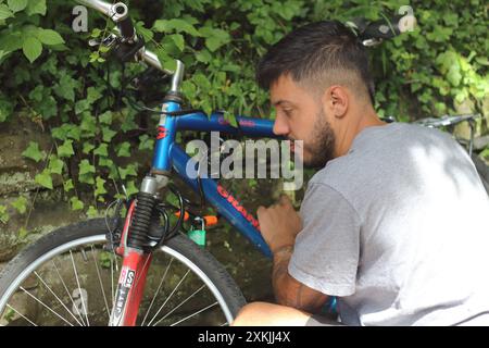 Ein dynamisches Bild, das einen jungen tätowierten Mann aufnimmt, während er sein altes Fahrrad freischaltet. Perfekt für Themen im Zusammenhang mit urbanem Leben, Radfahren und persönlichem Stil Stockfoto