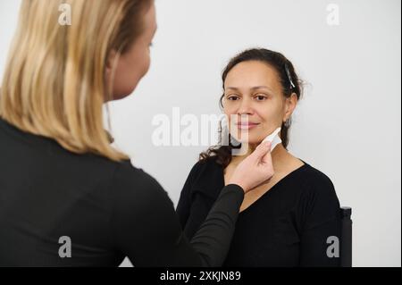 Ein Schönheitsexperte schminkt eine lächelnde Frau in einem Salon sorgfältig und betont dabei das Detail und die Fertigkeit der Kosmetik. Perfekt für Be Stockfoto