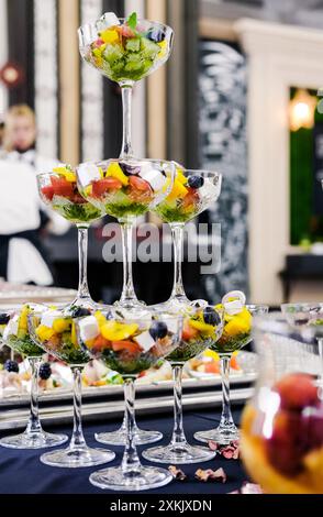 Nahaufnahme eleganter Glaswaren gefüllt mit einem bunten Gemüsesalat, angeordnet in einer gestuften Präsentation auf einem Tisch. Vertikales Foto. Stockfoto