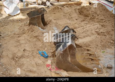 Abbildung der schweren Maschinen auf einer Baustelle mit zwei teilweise in Sand vergrabenen Baggerlöffeln Stockfoto