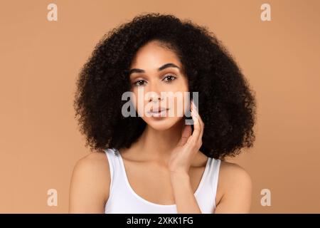 Eine junge Frau mit lockigem Haar posiert in weißem Tank Top Stockfoto