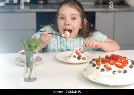 Das fröhliche kleine Mädchen isst Kuchen und steckt ihr ein großes Stück Dessert in den Mund. Ausgewählter Fokus. Hochwertige Fotos Stockfoto