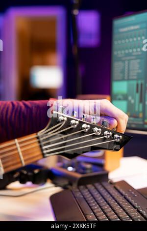 Ein erfahrener Musiker, der seine akustischen Gitarrensaiten abstimmt, um neue Audiodateien in einer Heimstudiosession aufzunehmen und dabei die Knöpfe im Einklang zu drehen. Songwriter produziert und bearbeitet neue Songs. Nahaufnahme. Stockfoto