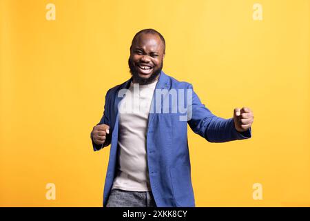 Porträt eines fröhlichen afroamerikanischen Mannes, der feiert und vor Aufregung Fäuste in die Luft wirft. Überfröhliche BIPOC-Person, die Erfolg genießt, jubelt und gestikuliert, Studiohintergrund Stockfoto