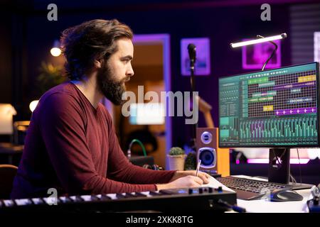 Songwriter macht sich Notizen, um neue Musik in seinem Studio zu kreieren, schreibt Texte und harmonische Elemente auf, bevor er seinen Song mit daw-Software aufnimmt, Akustik-Technik-Post-Production. Stockfoto