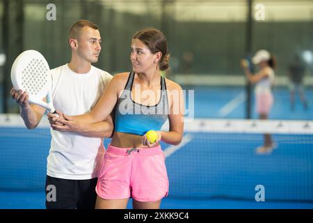 Das junge Mädchen lernt Padel unter der Leitung eines männlichen Trainers zu spielen Stockfoto