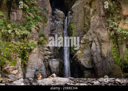 Ein Paar sitzt vor dem Wasserfall von Salto do Cabrito. Sao Miguel Insel auf den Azoren. Stockfoto