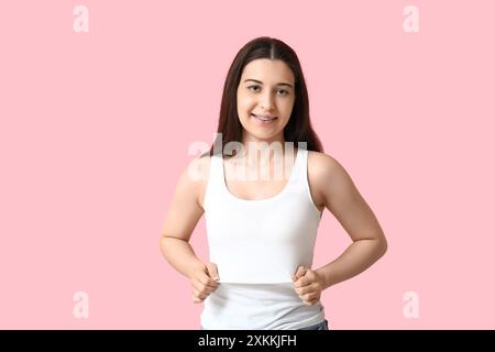 Hübsche junge Frau in stilvollem weißem Tanktop auf rosa Hintergrund Stockfoto