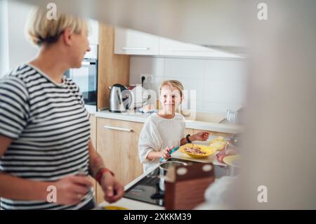 Mutter und Tochter genießen die warme Zeit zusammen in der modernen Küche, die Mahlzeiten zubereiten. Die Tochter lächelt herzlich, wenn sie dieses Kocherlebnis teilen. Perfekt für Stockfoto