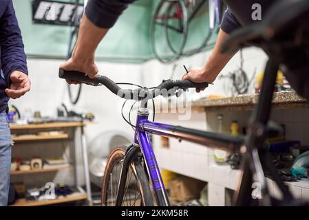 Nicht erkennbarer Servicetechniker, der ein Fahrrad in seiner Fahrradwerkstatt im Rahmen einer Wartung montiert. Echte Menschen bei der Arbeit. Stockfoto