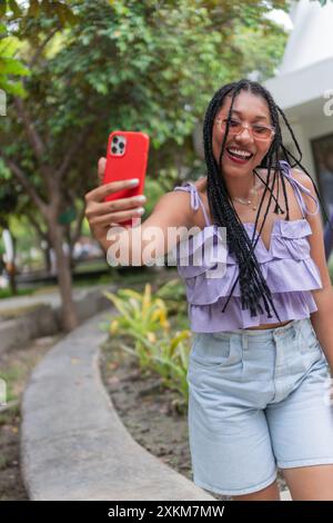 Afrikanische Frau lächelt, während sie Selfie mit dem Roten Telefon nimmt Stockfoto