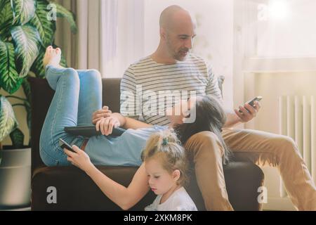 Glückliche Familie, die sich über Technologie auf dem Sofa zuhause verbündet, auf Telefonen und Tablets im Wohnzimmer surft. Genießen Sie die Bildschirmzeit zusammen mit einem Lächeln Stockfoto