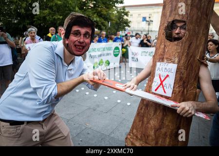 Madrid, Spanien. Juli 2024. Ein Demonstrant mit Maske und dem Gesicht von Jose Luis Martinez Almeida, Bürgermeister von Madrid, hält eine Säge neben einem Demonstranten, der als Baum verkleidet ist, während einer Demonstration gegen das Fällen von Bäumen auf der Plaza Santa Ana. Der Madrider Stadtrat plant, 30 Bäume auf der Plaza Santa Ana in Madrid zu Fällen, um die Tiefgarage umzubauen. Quelle: SOPA Images Limited/Alamy Live News Stockfoto