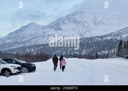 Delta Junction, Alaska - 14. Januar 2024: Menschen gehen auf dem Richardson Highway neben einem Parkplatz mit Bergen im Hintergrund auf einem kalten W Stockfoto