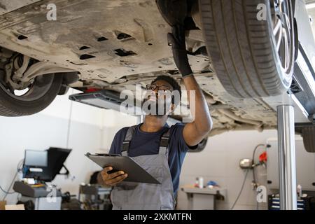 Automechaniker, der das Fahrwerk mit Klemmbrett überprüft Stockfoto