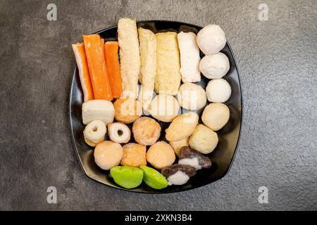 Ein schwarzes Tablett mit einer Vielzahl von Lebensmitteln, einschließlich einer Krabbe und einer grünen Kugel. Das Fach wird auf eine graue Oberfläche gestellt Stockfoto