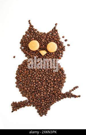 Kreative Eulenform aus Kaffeebohnen mit Makronen für Augen und Schnabel auf weißem Hintergrund. Stockfoto