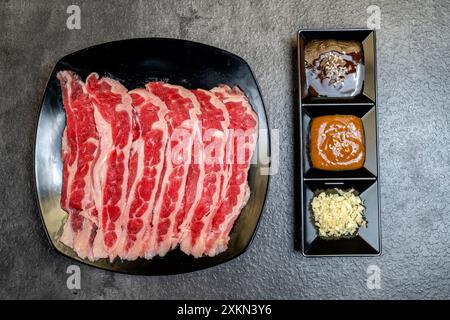 Ein Teller mit Fleisch steht auf einem Tisch mit drei kleinen Schüsseln Würzmittel. Das Fleisch ist in Scheiben geschnitten und er ist Rindfleisch. Die Schüsseln sind mit verschiedenen Saucen gefüllt, inkl. Stockfoto