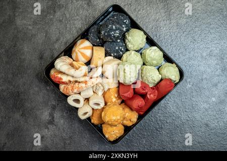 Ein schwarzes Tablett mit einer Vielzahl von Lebensmitteln, einschließlich einer Krabbe und einer grünen Kugel. Das Fach wird auf eine graue Oberfläche gestellt Stockfoto
