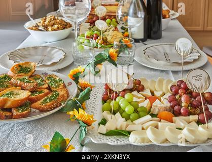 Ein eleganter Shavuot-Feiertagstisch mit Wein, Käse, Obst und Weihnachtsdekoration, bereit für ein traditionelles jüdisches Feiertagsessen. Happy Shavuot Inscript Stockfoto