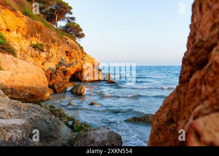 Pulsierende Küstenklippen treffen auf ruhiges Wasser und schaffen eine idyllische Landschaft. Das sanfte Licht unterstreicht die natürliche Schönheit der Küste von Tarragona. Stockfoto