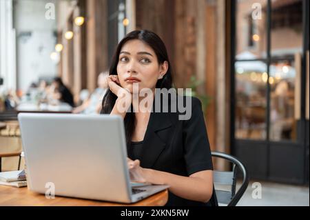 Eine unsichere, ernsthafte, nachdenkliche asiatische Geschäftsfrau in einem schwarzen Anzug schaut tief in Gedanken weg, besorgt um ihren Job, während sie von fern arbeitet Stockfoto
