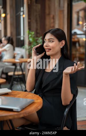 Eine selbstbewusste, elegante asiatische Geschäftsfrau telefoniert mit ihrem Kunden, während sie von einem Café aus in der Stadt aus im Freien arbeitet Stockfoto