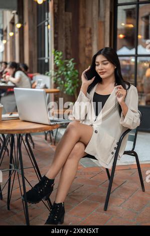 Eine selbstbewusste, elegante asiatische Geschäftsfrau telefoniert mit ihrem Kunden, während sie von einem Café aus in der Stadt aus im Freien arbeitet Stockfoto