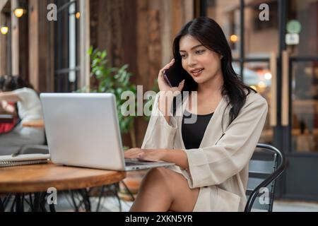 Eine selbstbewusste, wunderschöne asiatische Geschäftsfrau in modischer Kleidung spricht am Telefon mit ihrem Kunden, während sie von einem Café in der Stadt aus arbeitet Stockfoto