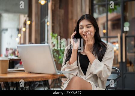 Eine wunderschöne, sorglose asiatische Geschäftsfrau spricht gern am Telefon, während sie an einem Tisch im Freien sitzt und in der Stadt arbeitet. p Stockfoto