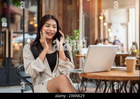 Eine wunderschöne, sorglose asiatische Geschäftsfrau spricht gern am Telefon, während sie an einem Tisch im Freien sitzt und in der Stadt arbeitet. p Stockfoto