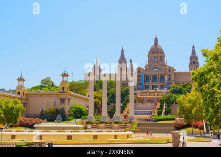 Barcelona, Spanien - 16. Juli 2024: Wunderschönes vier-Säulen-Denkmal und magischer Brunnen vor dem Palau Nacional umgeben von Grün. Stockfoto