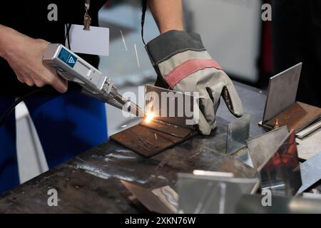 Junger weiblicher Schweißer, der mit handgehaltener Faserlaserschweißmaschine arbeitet. Selektiver Fokus. Stockfoto