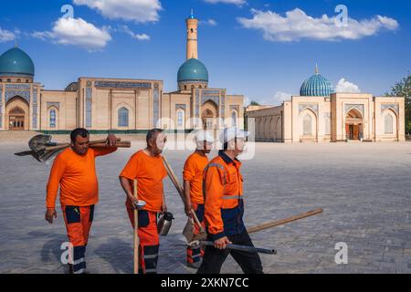 Gruppe von usbekischen männlichen Hausmeister in orangen Uniformen mit Schaufeln auf der Straße im Frühling auf dem Platz des Hazrati Imam Architekturkomplexes. Taschkent, Usbekistan - 17. April 2024 Stockfoto