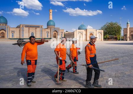 Gruppe usbekischer männlicher Hausmeister in orangen Uniformen mit Schaufeln auf der Straße im Frühling auf dem Platz des Hazrati Imam Architekturkomplexes. Taschkent, Usbekistan - 17. April 2024 Stockfoto