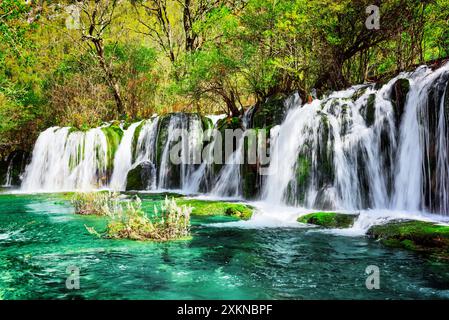 Wasserfall und azurblauer See mit kristallklarem Wasser inmitten grüner Wälder Stockfoto