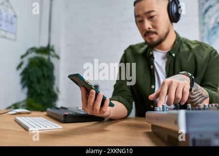 Ein junger asiatischer Mann mischt Musik in seinem Studio, in lässiger Kleidung, mit einem fokussierten Ausdruck. Stockfoto