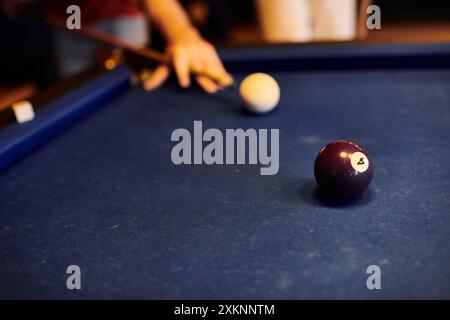 Eine Nahaufnahme einer Billardkugel auf einem blauen Filztisch mit einer verschwommenen Figur im Hintergrund. Stockfoto