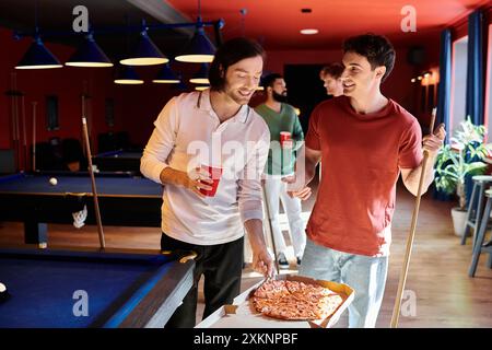 Freunde stehen an einem Billardtisch in ungezwungener Atmosphäre und genießen Pizza und Getränke mit Freunden. Stockfoto