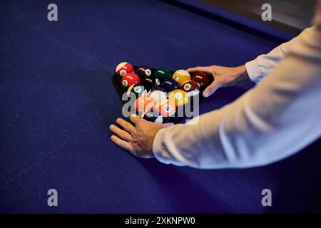 Ein Spieler arrangiert die Billardbälle in einem Dreieck auf dem mit Filz bedeckten Tisch und bereitet sich auf ein zwangloses Spiel mit Freunden vor. Stockfoto