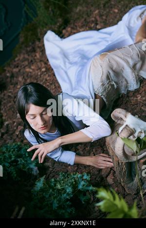 Eine Frau in fließenden weißen Gewändern streckt sich in einen Sumpf. Stockfoto